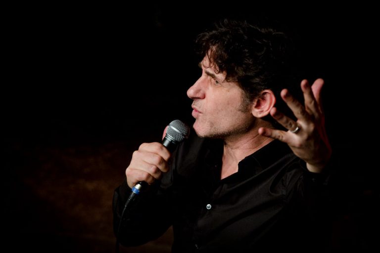 Tom Stade in profile at the mic, gesturing