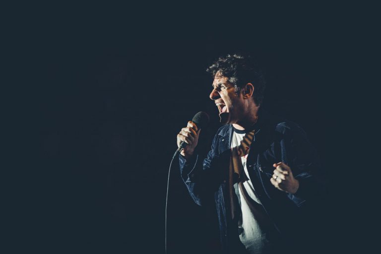 Tom Stade on stage with a microphone under blue light