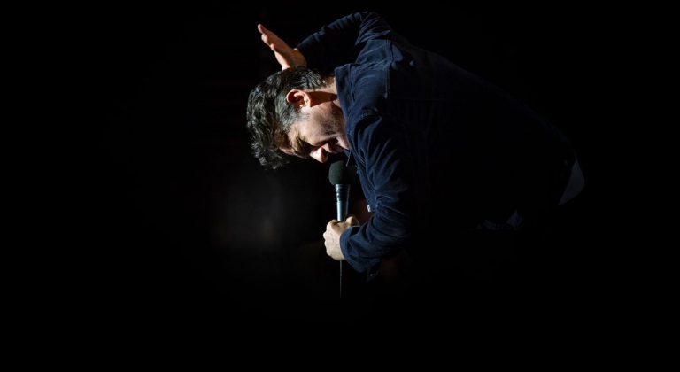 Tom Stade leaning back on stage, lit from behind