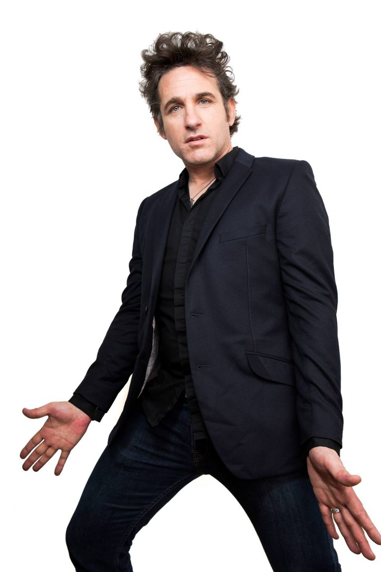 Tom Stade in a dark suit, full length on white