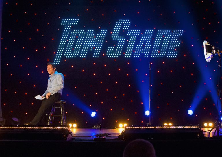 Tom Stade on stage with his name in lights behind him