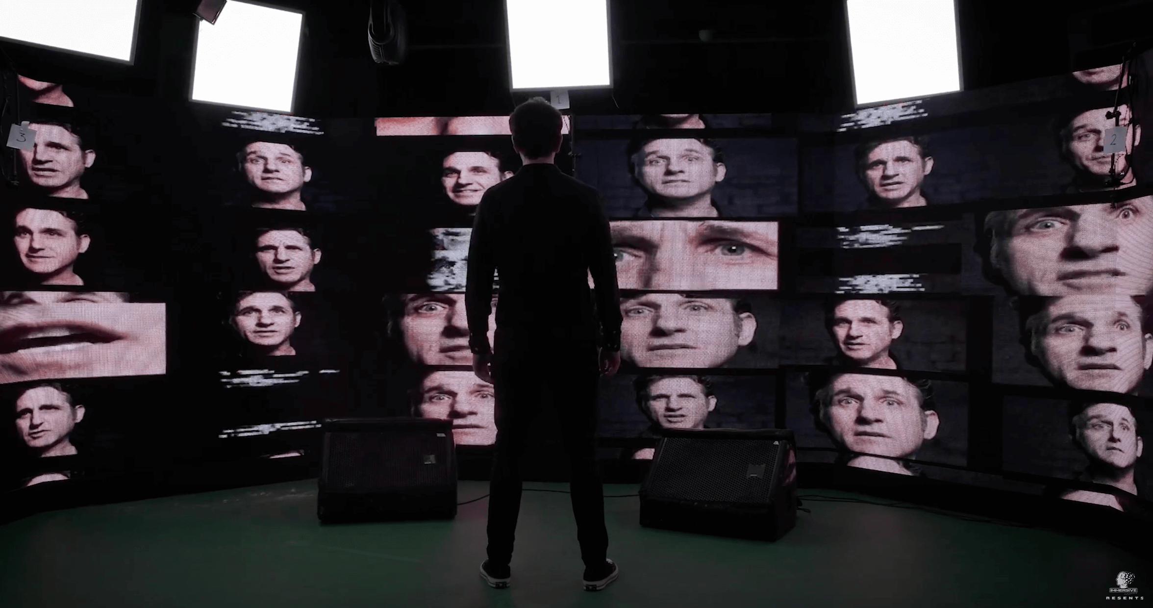 A man stares at a wall of various TV screens. They all have Tom Stade's face on them