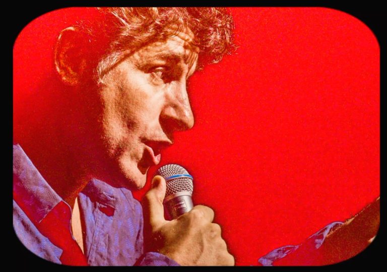 Tom Stade at the mic against a red background